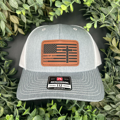 Leatherette patch hat engraved with "Man of God, Husband, Dad" over an American flag and cross. 