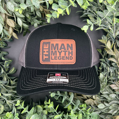 Black cap with rawhide patch 'The Man Myth Legend' logo on a green leafy background